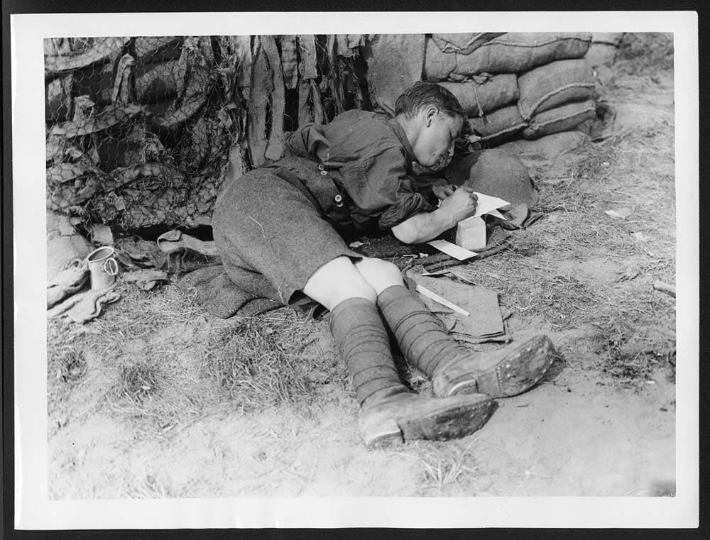 Soldat allongé écrivant une lettre près d’un mur de sacs de sable, 1917